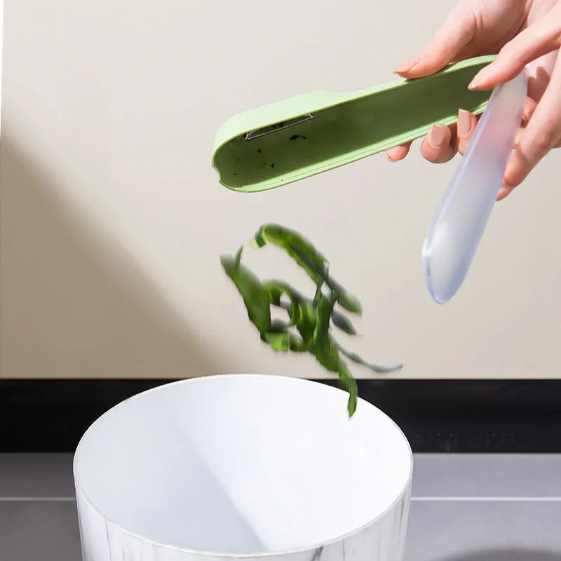Dark green kitchen peeler with stainless steel blade inside its open storage tube on a counter.
