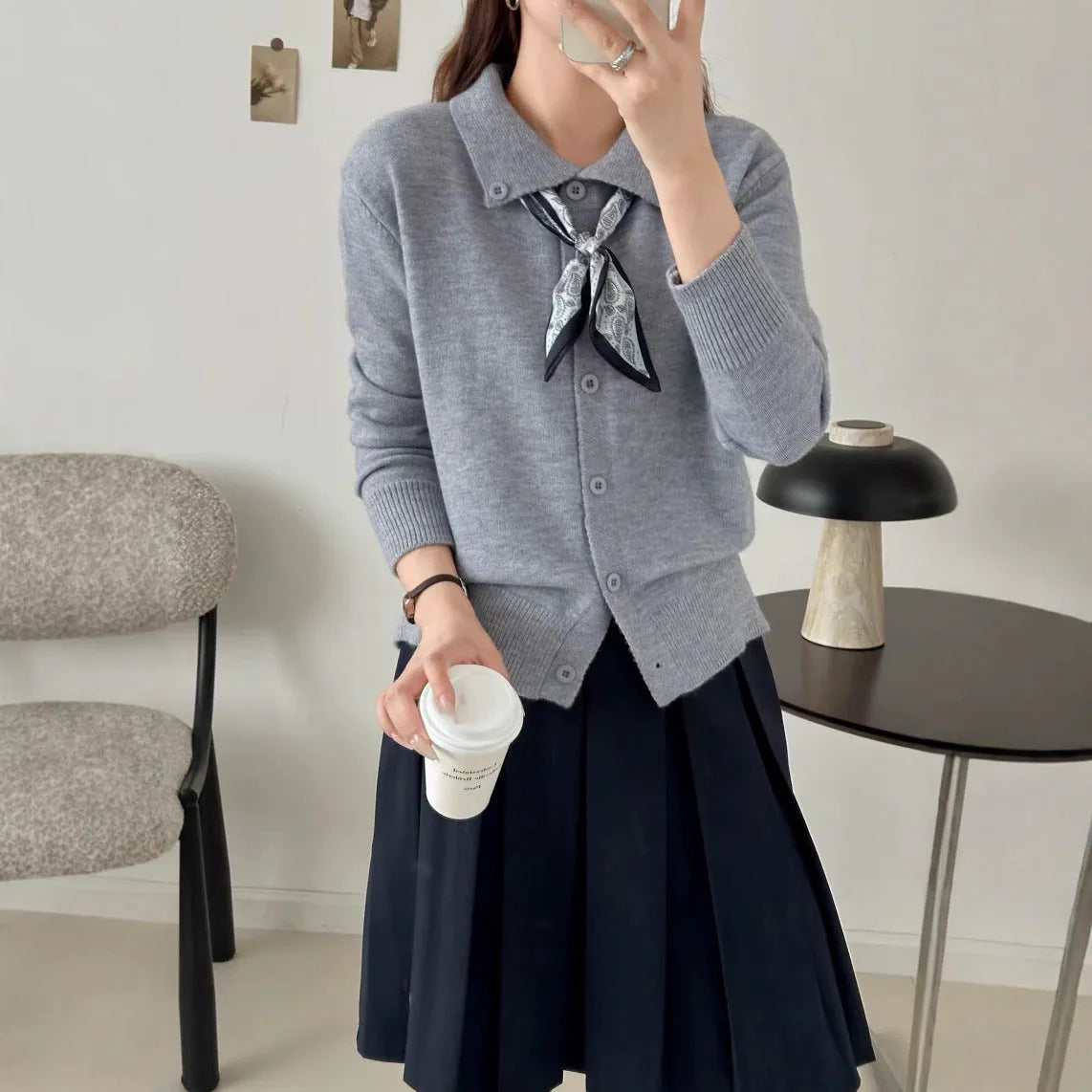 Beige acrylic cardigan with lapel scarf collar and splicing detail on a hanger.