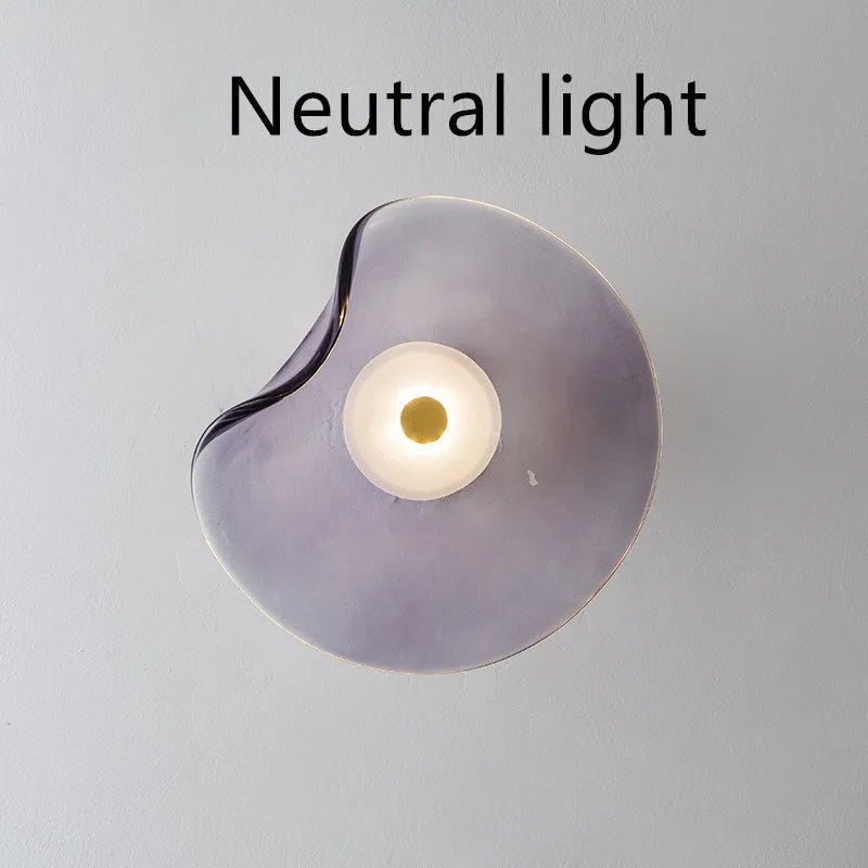 Round glass wall lamp in cognac colour mounted beside a bed with warm light illumination