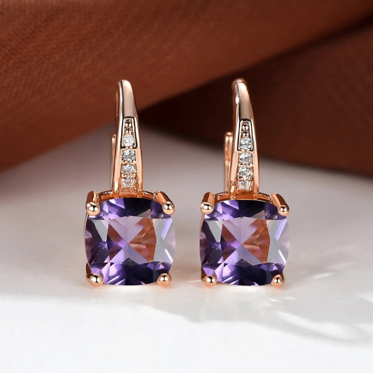 Geometric copper ear hook with round element and inlaid square zircon stone, shown in a golden colour.