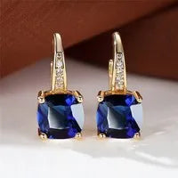 Geometric copper ear hook with round element and inlaid square zircon stone, shown in a golden colour.