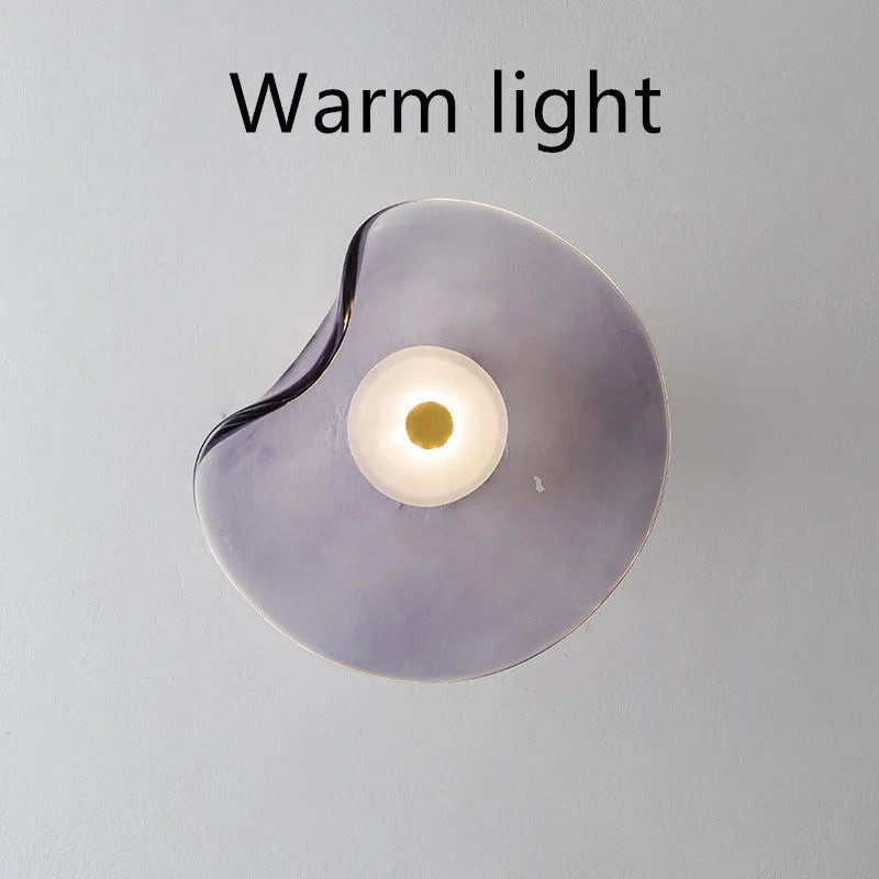Round glass wall lamp in cognac colour mounted beside a bed with warm light illumination