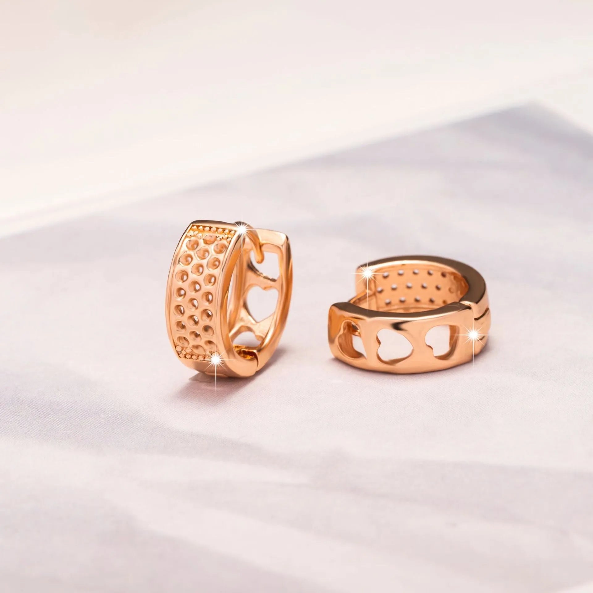 A pair of rose gold women's earrings with three hollowed-out heart shapes in a circular design.