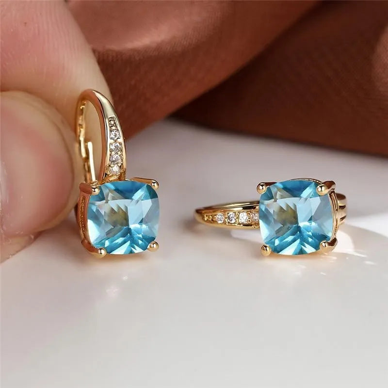 Geometric copper ear hook with round element and inlaid square zircon stone, shown in a golden colour.