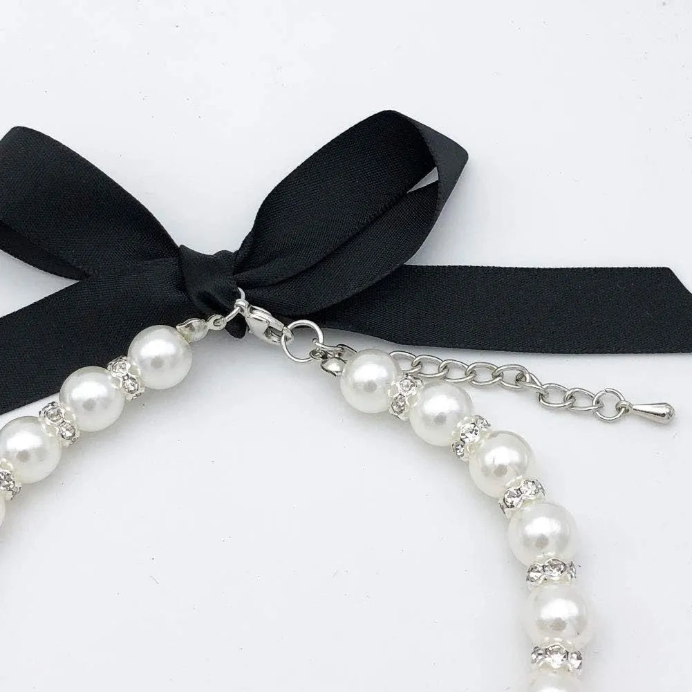 Small dog wearing adjustable pearl necklace with rhinestones and ribbon bow decorative collar