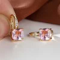 Geometric copper ear hook with round element and inlaid square zircon stone, shown in a golden colour.