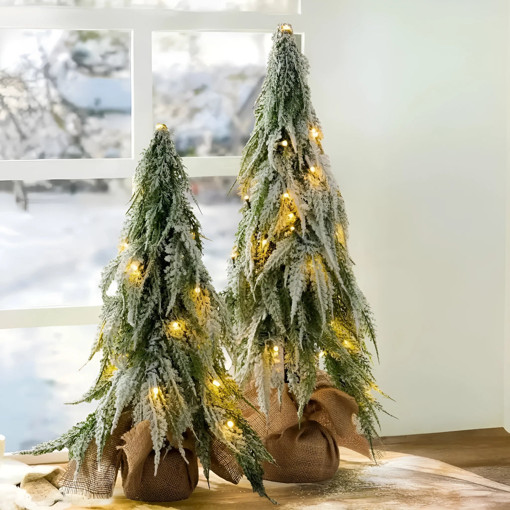 Small 24-inch white artificial Christmas tree with built-in LED lights and simulated snow sprayer on a desktop.