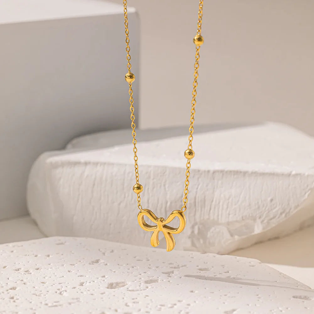 Gold coloured titanium steel necklace with a bow charm on a cross chain.
