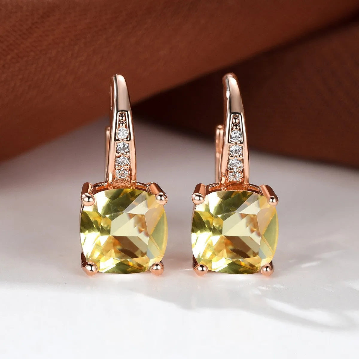 Geometric copper ear hook with round element and inlaid square zircon stone, shown in a golden colour.