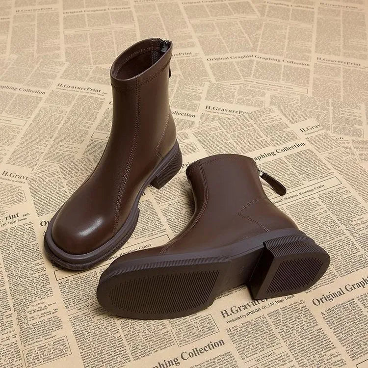 Women's black ankle boots with flat heel, round toe, and back zip fastening on wooden floor