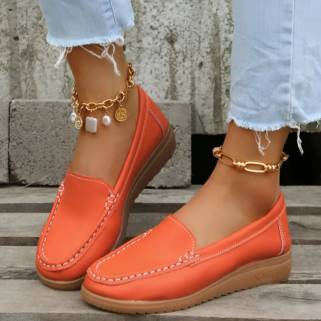 Women's flat slip-on loafers in PU leather, showing colour options and round toe design with decorative stitching.