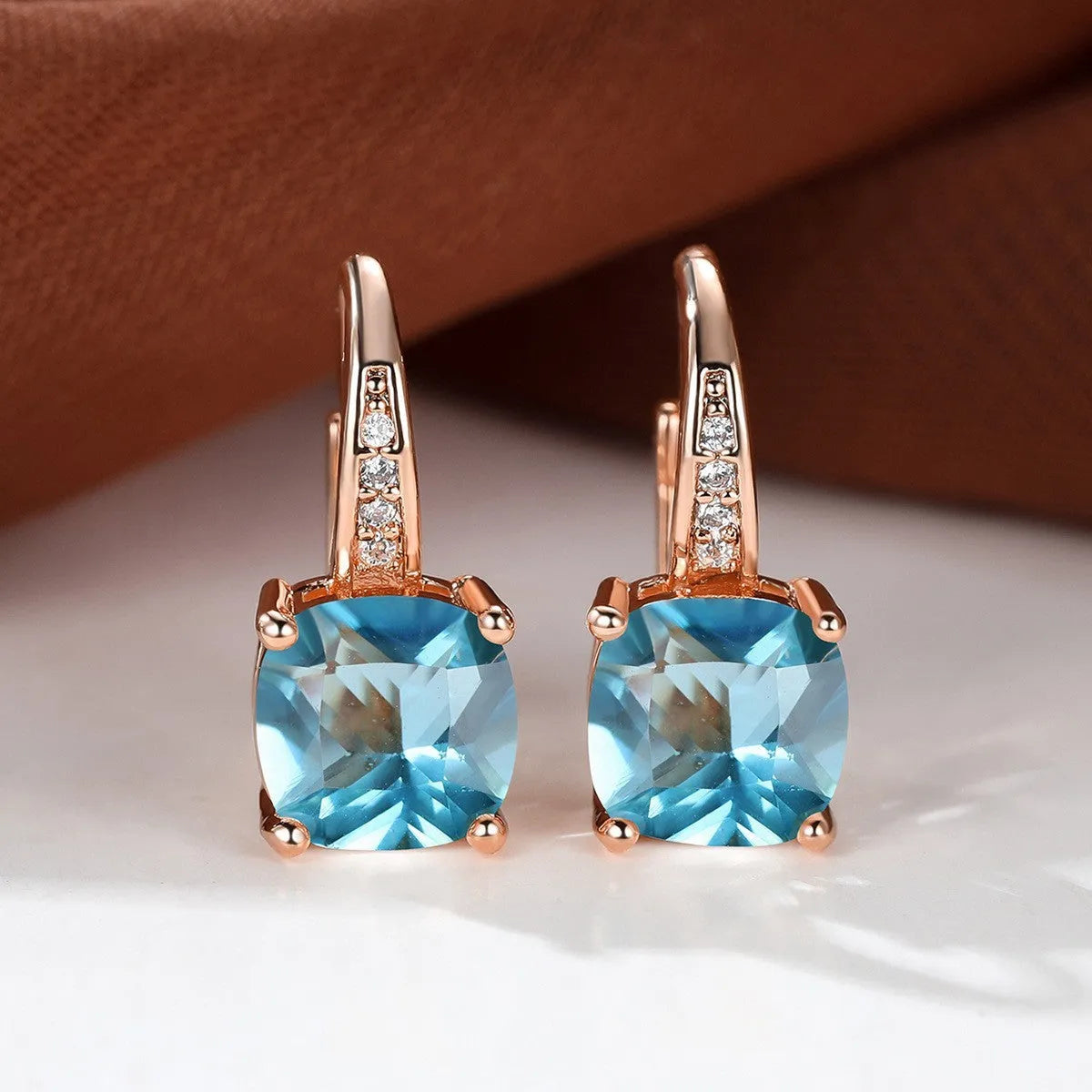 Geometric copper ear hook with round element and inlaid square zircon stone, shown in a golden colour.